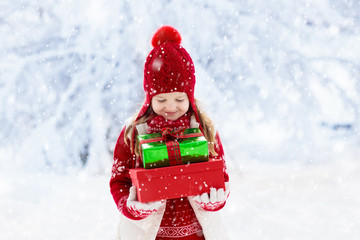 Child with Christmas present in snow. Kids gifts