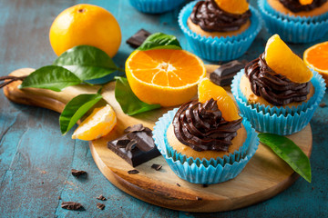 Orange Cupcakes with Chocolate Cream and Fresh Tangerines on a blue stone or concrete table.