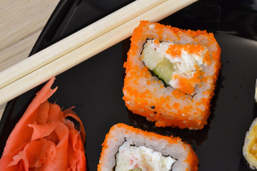 Sushi and rolls on a black plate with chopsticks.