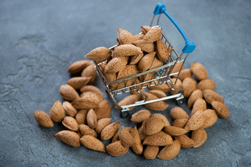 Decorative shopping cart with unpeeled almonds over blue stone background, studio shot