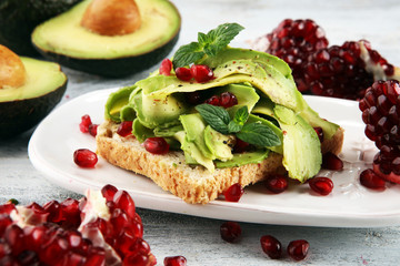 sliced avocado and ripe pomegranates on toast bread with spices and avocado.