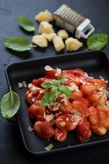 Close-up of potato gnocchi served with tomato sauce, parmesan cheese and fresh green basil in a cast-iron tray