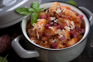 Close-up of a pan with potato gnocchi served with ground meat, salami and parmesan, selective focus