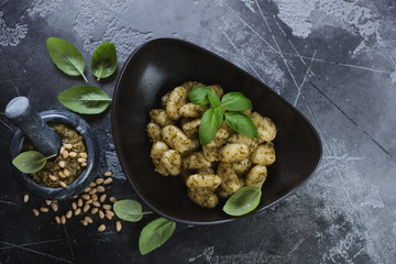 Top view of potato gnocchi served with basil pesto sauce in a black bowl, grey concrete background, horizontal shot