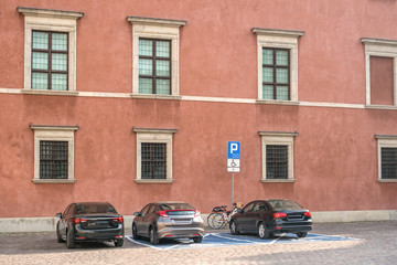 Fototapeta na wymiar Three cars are parked on a square in the historic part of the city near the sign disabled parking.