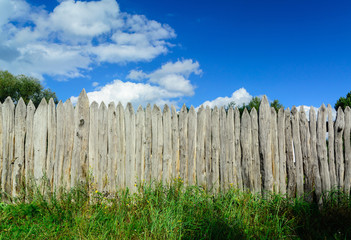 Obraz premium An old log fence and a blue sky with clouds. Security and fencing. Protection against thieves