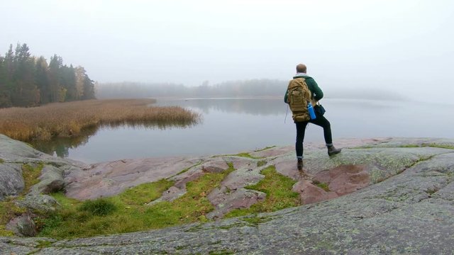 A middle-aged man walking on a rocky shore of the sea on a misty autumn morning and watching wildlife through binoculars. Slow motion
