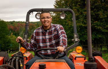 Young man on a tractor on a farm with mountains behind him