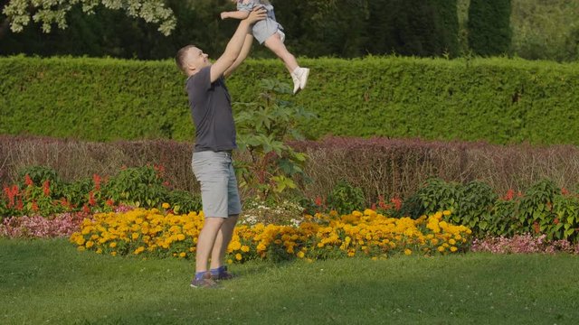 Father throwing baby girl in the air in the summer light in park. Baby have fun. Slow motion. Happy family concept. Baby emotions - laughing. 