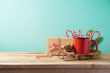 Christmas background with cup on sledges, candy cane and gift box on wooden table