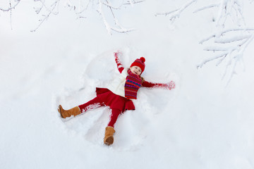 Child making snow angel. Kids winter outdoor fun.
