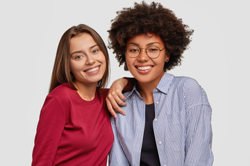 Friendly multiethnic girls have fun together, rejoice successful day at work, have toothy smiles,...