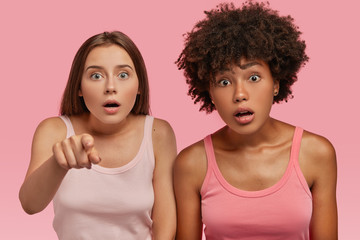 Emotional mixed race women have shocked gaze directly at camera, point, hold breath from shock,...