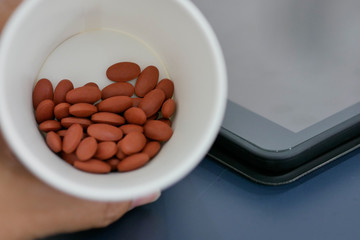 Hand holding cup of pills with blur tablet background.