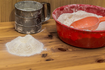 the flour is poured on a wooden surface on which there is a glass of flour and a red bowl of flour