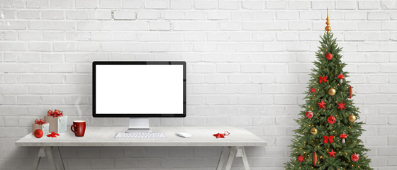 Computer display with isolated, blank screen for mockup on desk. Christmas tree and gifts beside. White brick wall in background.