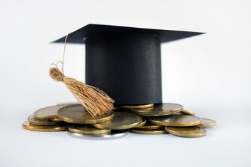Graduation cap on saving coins for concept finance and education scholarships. Graduation mortarboard and golden coins on white background, concept investment education, close up, selective focus, cop