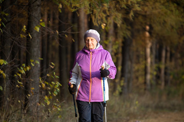 A woman over the age of 65 is engaged in Nordic walking in the fresh air.