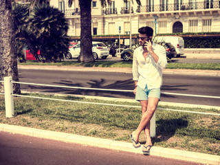 Attractive fit athletic young man soaking in the sun on seaside boardwalk or seafront, wearing white shirt in Nice, France on the French Riviera