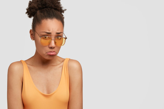 Unhappy black woman sulks from sadness, purses lower lip, has displeased facial expression, recieves bad news, isolated over white background with copy space for your advertisement or promotion