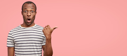 Omg and advertisement concept. Indoor view of astonished black African man wears round glasses,...