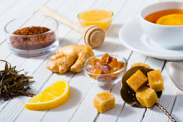 cup of tea, different leaves, honey, lemon ginger and brown sugar on white wooden table background
