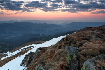 Naklejka na ściany i meble The meadow with the rocks and yellow grass. Landscape of high peaks of mountains, pink sunrise at the horizon.