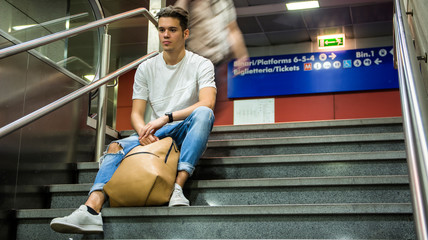 Handsome young man sitting on stairs' marble steps, backpack next to him