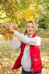 cheerful young woman throwing autumn leaves in forest