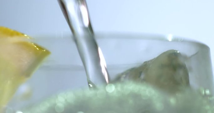 Close up of a refreshing drink being poured into a glass with ice and lemon