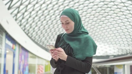 Young muslim woman in a hijab stands in a shopping center and uses the phone,slow mo