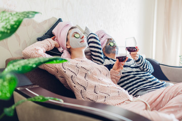 Mother and her adult daughter applied facial masks and cucumbers on eyes. Women chilling while...