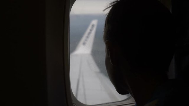 boy flies in an airplane and looks out the window