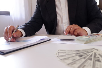 Businessman using calculator with money on the desk.