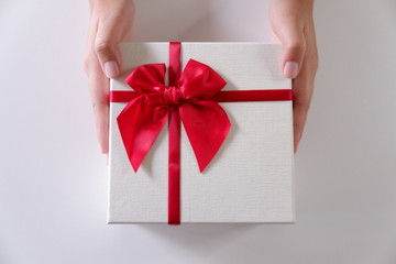 Close-up women hands sending white gift box with red ribbon on white background.