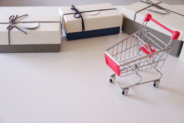 Close-up of gift boxes and shopping cart  on white desk.