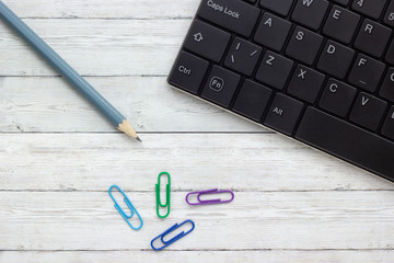 Keyboard, pencil and paper clips on wooden background