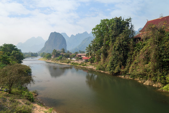 Scenic view of the Nam Song River, Pha Tang village and limestone mountains near Vang Vieng, Vientiane Province, Laos, on a sunny day.