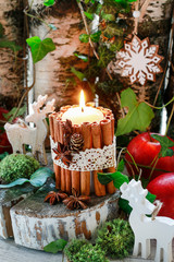 Candle decorated with cinnamon sticks, moss, ivy leaves and wooden deers