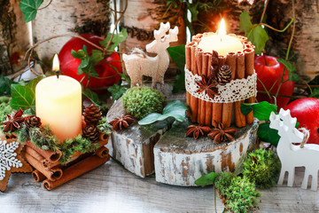 Candle decorated with cinnamon sticks, moss, ivy leaves and wooden deers