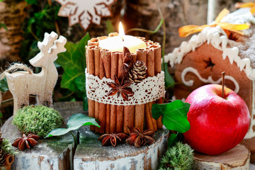 Candle decorated with cinnamon sticks, moss, ivy leaves and wooden deers