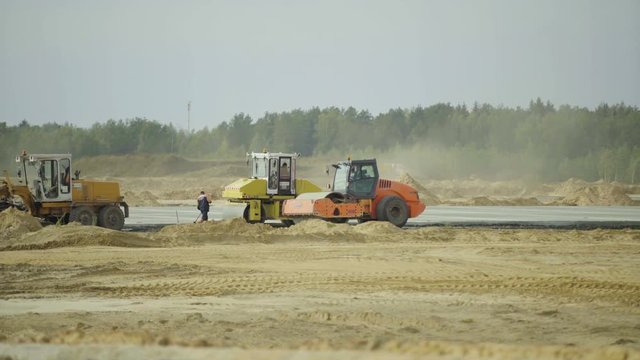 Construction, concreting of airport runways roads, highway. Men, workers working with asphalt paver. Roadroller, construction machinery works on new runway construction of national airport Minsk, MSQ