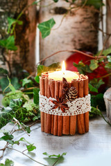 Candle decorated with cinnamon sticks, moss, ivy leaves and wooden deers