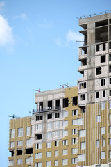 Process of mounting insulation on apartment building facade in new modern urban house over blue sky with clouds closeup