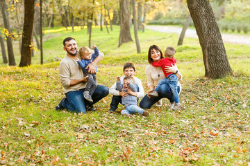 Fototapeta premium Lovely big family with four cheerful sons are playing on yellow autumn leaves in park