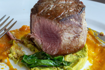 Close up on a filet mignon steak on a white plate  with peas and  butternut squash partial view of a fork puree 