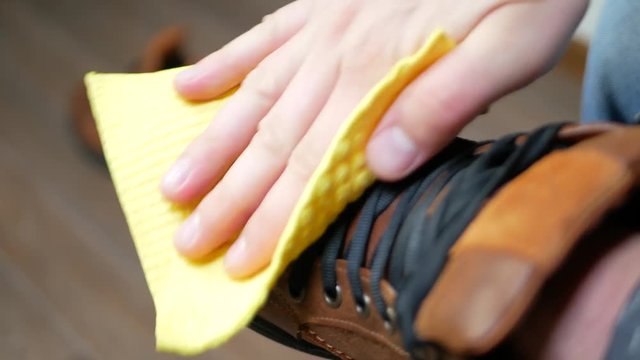 Hand dusting brown leather shoes with a yellow rag from dust and dirt. Autumn or winter shoes concept