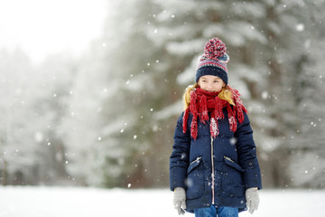 Adorable little girl having fun in beautiful winter park. Cute child playing in a snow.