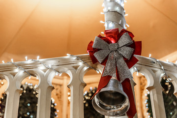 Cute outdoor Christmas ornament with a bell and a bow, hanging on a banister