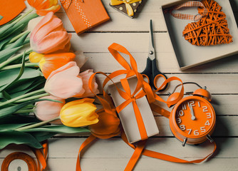 Gift boxes, scissors and flowers with alarm clock on white wooden backgrorund